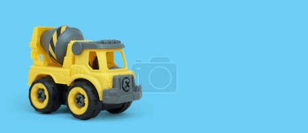 Téléchargez les photos : Jouet de camion malaxeur en plastique jaune isolé sur fond bleu avec espace de copie pour la bannière du magasin de jouets. - en image libre de droit