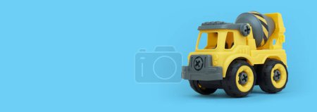 Téléchargez les photos : Jouet de camion malaxeur en plastique jaune isolé sur fond bleu avec espace de copie pour la bannière du magasin de jouets. - en image libre de droit