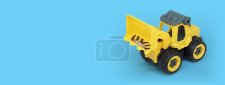 Téléchargez les photos : Jouet bulldozer en plastique jaune isolé sur fond bleu avec espace de copie pour bannière de magasin de jouets - en image libre de droit