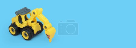 Téléchargez les photos : Jouet de forage tracteur en plastique jaune isolé sur fond bleu avec un espace de copie pour le texte ou la bannière de magasin de jouets - en image libre de droit