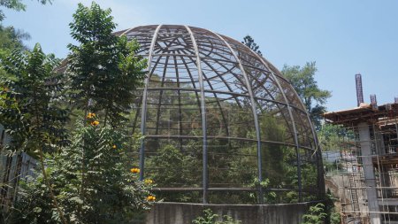 Foto de Aviario de cúpula metálica grande para la conservación de aves junto a un sitio de construcción de edificios - Imagen libre de derechos