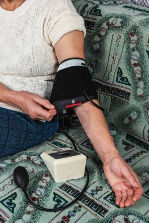 Photo for Grandma takes her blood pressure sitting on the couch - Royalty Free Image