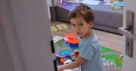 Photo for Opened door to boy child room unnoticed and see kid play with toys. Surprised child looks at somebody who silently and unexpectedly entered room. High quality photo - Royalty Free Image