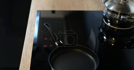 Schalten Sie schwarze Induktions- oder elektrische Kochfläche mit Pfanne ein. Komfortable Küche mit modernem Kochgerät ausgestattet. Hochwertiges Foto
