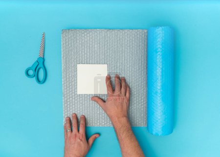 Photo for Caucasian adult male hands packaging blank white square paper with bubblewrap and scissors - Royalty Free Image