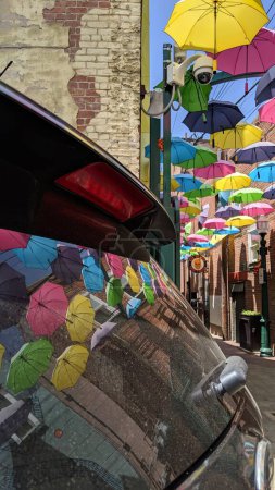Photo for Redlands, California - April 27, 2019: Colorful Umbrellas Hanging Above Orange Street Alley in Downtown Redlands. A reflection can be seen in the back window of a vehicle. - Royalty Free Image