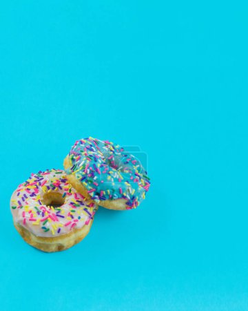 Photo for Two donuts with blue and white icing and colorful sprinkles on a plain turquoise blue background with room for copy space. - Royalty Free Image