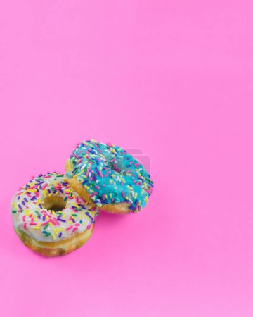 Photo for Two donuts with blue and white icing and colorful sprinkles on a plain bright pink background with room for copy space. - Royalty Free Image