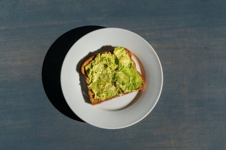 Photo for Avocado toast on a white plate sitting on a concrete countertop in bright sunlight with hard shadows - Royalty Free Image