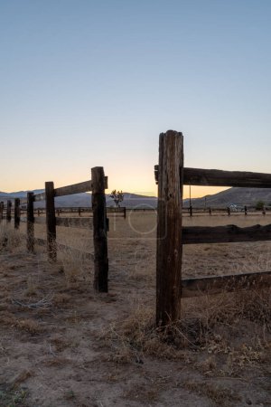 Cerca de madera vieja en un rancho del desierto de California en Pioneertown con una puesta de sol y montañas en el fondo.
