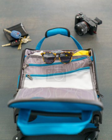 Photo for Small blue luggage bag with sunglasses, camera, wallet, and keys. Ready for a vacation holiday getaway. - Royalty Free Image