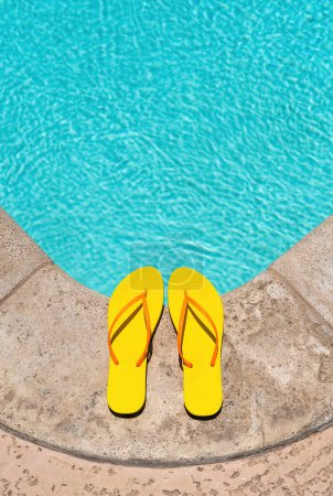 Photo for Yellow Flip Flops at the edge of a swimming pool deck - Royalty Free Image