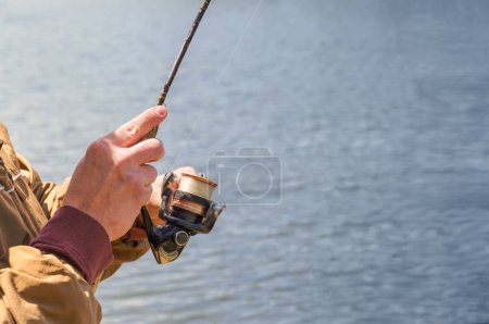 Téléchargez les photos : Gros plan d'un jeune homme rentrant avec une vieille canne à pêche et enroulant au bord d'un lac. Chambre pour l'espace de copie. - en image libre de droit