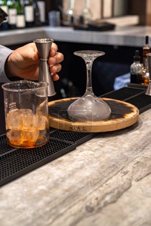 Photo for Bartender holding a jigger and making a smoked whiskey cocktail drink with glass beaker and an upside down cocktail glass in a bar - Royalty Free Image