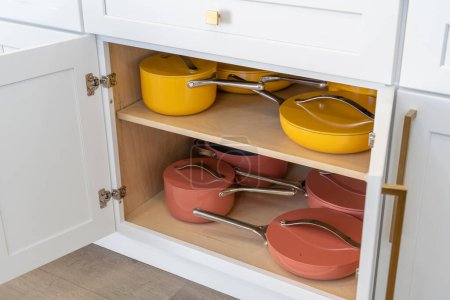 Colorful cookware of pots, pans, and skillets in white kitchen cabinet