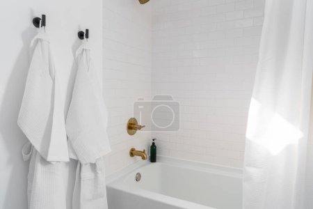 Photo for White home bathroom shower tub with brass hardware and bath robes vacation rental - Royalty Free Image