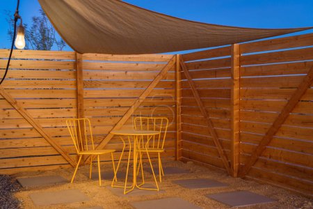 Photo for Patio with modern yellow bistro set protective sun shade canopy and wood privacy fence in the evening dusk - Royalty Free Image