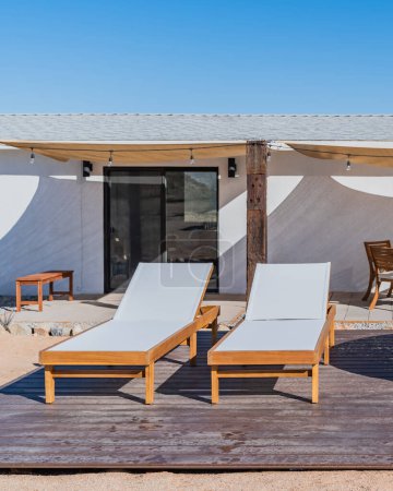 Two white wood outdoor chaise lounge chairs on a backyard deck
