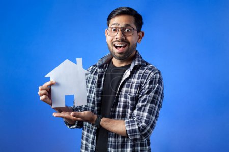 Photo for Indian ethnicity, excitement, model home. Surprised student showing paper house craft. - Royalty Free Image