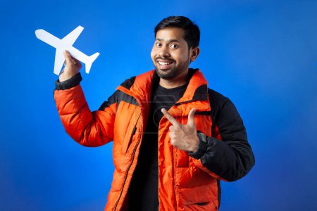 Photo for Travel destination, journey, airport. A young man pointing finger to the paper cutting plane with toothy smile. - Royalty Free Image