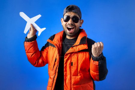 Photo for Airplane, tourist, journey. Cheerful man holding paper cutting plane, isolated on blue background. - Royalty Free Image