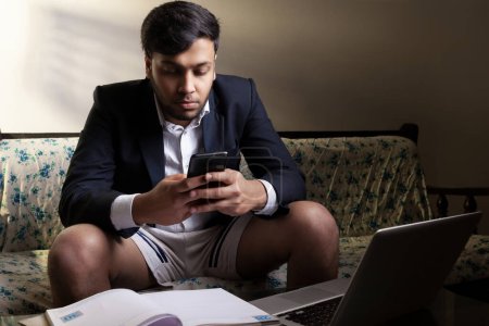 Photo for Indian man late night working from home wearing half suit using mobile and laptop - Royalty Free Image