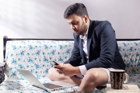 Photo for Half suit man using mobile phone while working on laptop at living room - Royalty Free Image