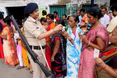 Foto de 08 de julio de 2023, Howrah, India: Una oficial de policía chocando la identificación de votantes mientras la gente hace cola en un centro electoral para emitir su voto en las elecciones locales o panchayat de Bengala Occidental, en las afueras de Calcuta el 8 de julio de 2023 en Calcuta, India - Imagen libre de derechos