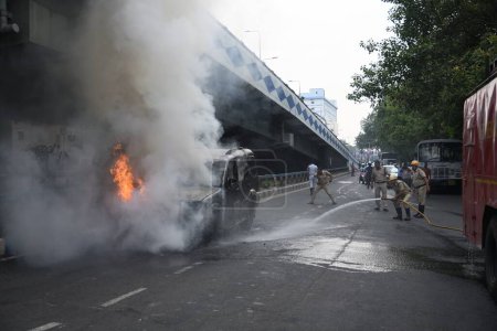 Photo for May 31, 2023, Kolkata, India. Fire fighters throwing water to the burning mid-size sport utility vehicle (SUV) as it catches fire due to overheat on the busy AJC Bose Road. No death or injury suffered in the accident - Royalty Free Image