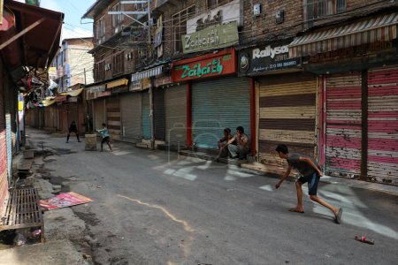 Photo for August 15,2023, Srinagar Kashmir, India : Boys play cricket past closed shops during India's 77th Independence Day celebrations in Srinagar - Royalty Free Image