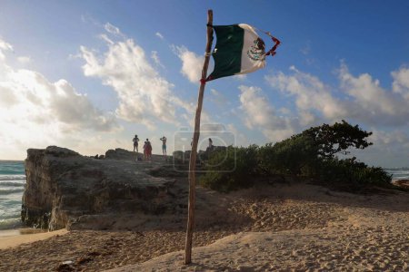 Téléchargez les photos : Un drapeau mexicain brisé sur le rivage d'une plage des Caraïbes mexicaines à l'aube - en image libre de droit