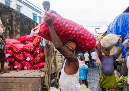 Téléchargez les photos : 17 juillet 2023, Kolkata, Inde : Les travailleurs de la base quotidienne transportent une charge de légumes sur un marché aux légumes de gros. - en image libre de droit