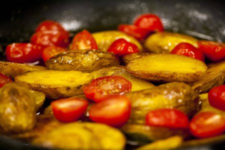 Téléchargez les photos : Assiette de tranches de pommes de terre cuites au four accompagnée de tomates cerises - en image libre de droit