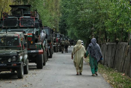 Photo for September 15,2023, Srinagar Kashmir, India : Women walk past Indian army vehicles during the fierce gun-battle between militants and security forces which entered second day in Gadole village of Kokernag in Anantnag district - Royalty Free Image