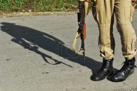 Téléchargez les photos : 19 septembre 2023, Srinagar Cachemire, Inde : L'ombre d'un fusil d'assaut d'un policier est projetée près du site de la fusillade entre les militants et les forces de sécurité dans le village Gadole de Kokernag dans le district d'Anantnag - en image libre de droit