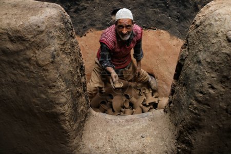 Photo for November 02,2023, Srinagar Kashmir, India : Abdul Salam Kumar, a Kashmiri Muslim potter takes out earthen lamps from an oven at his home workshop ahead of the Diwali festival, on the outskirts of Srinagar - Royalty Free Image