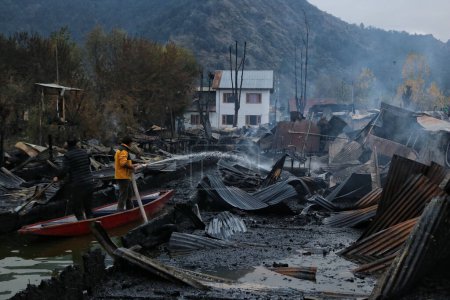 Téléchargez les photos : 11 novembre 2023, Srinagar Cachemire, Inde : Un homme du Cachemire travaille à éteindre un incendie qui a détruit plusieurs péniches au lac Dal à Srinagar - en image libre de droit