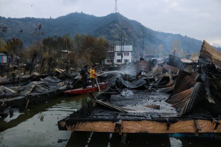 Téléchargez les photos : 11 novembre 2023, Srinagar Cachemire, Inde : Un homme du Cachemire travaille à éteindre un incendie qui a détruit plusieurs péniches au lac Dal à Srinagar - en image libre de droit