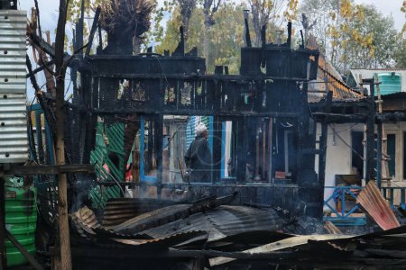 Téléchargez les photos : 11 novembre 2023, Srinagar Cachemire, Inde : Un homme du Cachemire regarde les péniches détruites dans un incendie au lac Dal à Srinagar - en image libre de droit