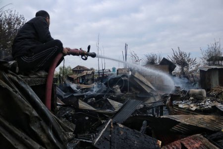 Téléchargez les photos : 11 novembre 2023, Srinagar Cachemire, Inde : Un homme du Cachemire travaille à éteindre un feu qui a détruit plusieurs péniches au lac Dal à Srinagar. Un incendie massif a éclaté dans les péniches dans le centre touristique du lac Dal à Srinagar - en image libre de droit