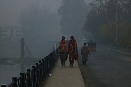 Téléchargez les photos : 23 novembre 2023, Srinagar Cachemire, Inde : Les gens marchent le long d'une route lors d'une matinée brumeuse à Srinagar. Le Cachemire a été témoin de conditions météorologiques brumeuses et froides avec Srinagar enregistrant la nuit la plus froide de la saison à moins 1,8 degré Celsius - en image libre de droit