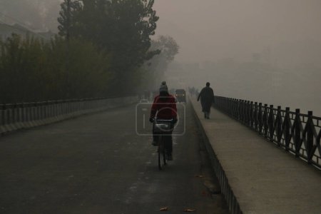 Téléchargez les photos : 23 novembre 2023, Srinagar Cachemire, Inde : Les gens marchent le long d'une route lors d'une matinée brumeuse à Srinagar. Le Cachemire a été témoin de conditions météorologiques brumeuses et froides avec Srinagar enregistrant la nuit la plus froide de la saison à moins 1,8 degré Celsius - en image libre de droit