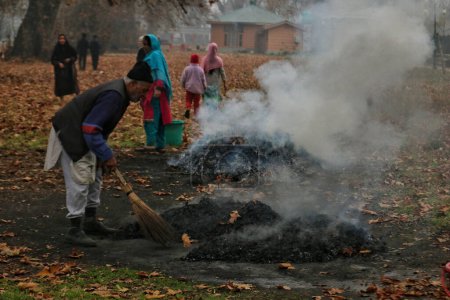Téléchargez les photos : 27 novembre 2023, Srinagar Cachemire, Inde : Une femme du Cachemire brûle des feuilles sèches de chinar à Srinagar. Kashmiris ces jours-ci recueillir des feuilles séchées tombées des arbres afin de les brûler pour produire du charbon de bois à utiliser comme combustibles - en image libre de droit