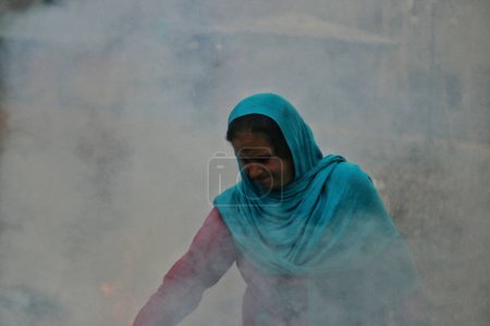 Photo for November 27,2023, Srinagar Kashmir, India : A Kashmiri woman burns dry chinar leaves in Srinagar. Kashmiris in these days collect dried leaves fallen from trees in order to burn them to produce charcoal to use as combustibles - Royalty Free Image