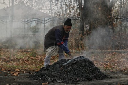 Téléchargez les photos : 27 novembre 2023, Srinagar Cachemire, Inde : Une femme du Cachemire brûle des feuilles sèches de chinar à Srinagar. Kashmiris ces jours-ci recueillir des feuilles séchées tombées des arbres afin de les brûler pour produire du charbon de bois - en image libre de droit