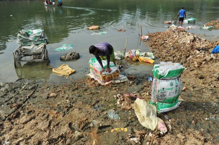 Téléchargez les photos : 10 décembre 2023 Sylhet-Bangladesh : Des travailleurs risquent leur vie pour laver des sacs de ciment dans l'eau de la rivière Surma à Sylhet, au Bangladesh. En outre, comme il nuit à leur santé à long terme - en image libre de droit