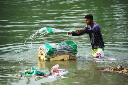 Téléchargez les photos : 10 décembre 2023 Sylhet-Bangladesh : Des travailleurs risquent leur vie pour laver des sacs de ciment dans l'eau de la rivière Surma à Sylhet, au Bangladesh. En outre, comme il nuit à leur santé à long terme - en image libre de droit