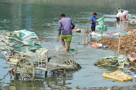 Téléchargez les photos : 10 décembre 2023 Sylhet-Bangladesh : Des travailleurs risquent leur vie pour laver des sacs de ciment dans l'eau de la rivière Surma à Sylhet, au Bangladesh. En outre, comme il nuit à leur santé à long terme, la poussière de plastique remplit l'eau et le lit de la rivière - en image libre de droit