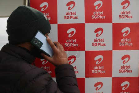 Photo for December 12,2023, Srinagar Kashmir, India : A man talks on his Mobile phone past logo of Airtel 5G Plus is seen during live 5G plus experience in Srinagar. Airtel announced the launch of its cutting edge 5G services - Royalty Free Image