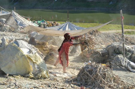 Photo for 19 December 2023 Sylhet-Bangladesh: A  young  boy with his mother working for an extra income for family are risking their lives working in the dust of the cement bags beside of Surma River in Sylhet, Bangladesh - Royalty Free Image
